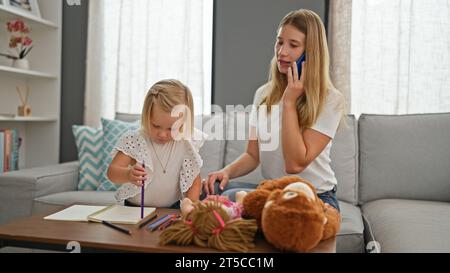 Entspannte Mutter-Tochter-Bindung, kaukasische Mutter und kleines Mädchen zeichnen auf dem Notebook und unterhalten sich zu Hause über das Smartphone ernsthaft Stockfoto