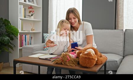 Herzzerreißende Szene zu Hause mit kaukasischen Mutter und Tochter, gemütlich auf dem Sofa im Wohnzimmer, zusammen lächelnd, während sie in ihre Digitala tauchen Stockfoto