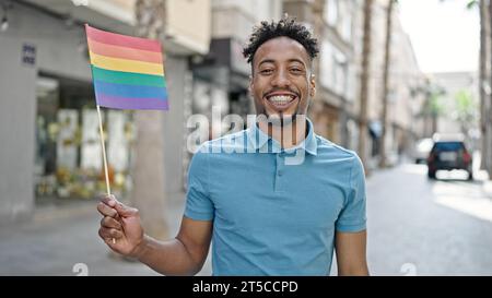 afroamerikaner lächelt zuversichtlich und hält Regenbogenfahne auf der Straße Stockfoto