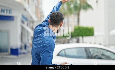 Junger hispanischer Mann hält mit erhobener Hand auf der Straße ein Taxi an Stockfoto