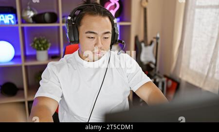 Konzentrierter junger chinese, ein Streamer für Technik, der sich ernsthaft in ein futuristisches digitales Spiel in der Nacht im Spielzimmer vertieft hat. Stockfoto