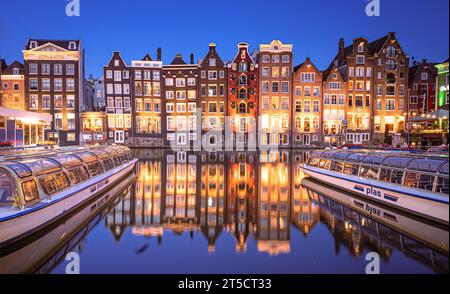Die Tanzhäuser Damrak Amsterdam in der Nacht mit Booten und Reflexion von Häusern im Wasser Niederlande Stockfoto