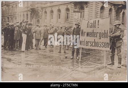 "Strassenszene aus den Revolutionstagen Berlins" / "Straßenszene aus den revolutionären Tagen Berlins": Straßensperre oder militärischer Kontrollpunkt auf den Straßen Berlins während der Deutschen Revolution von 1918 bis 1919, nach dem Ersten Weltkrieg. Zwei uniformierte Soldaten halten eine große Nachricht, auf der steht: "Halt! Wer weitergeht wird erschossen“ / „Stopp! Jeder, der weitermacht, wird erschossen. Andere Soldaten sind im Hintergrund, die eine Gruppe von Männern (einschließlich eines Matrosen) daran hindern, vorbei zu gehen Stockfoto