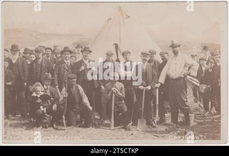 Bradford Back to the Land Pioneers, 1906: Foto von Yorkshire-Mitgliedern der Back to the Land-Bewegung in ihrem Lager, Klondyke Villa, mit Zelt, Spitzhacken und Pik. Im Juli 1906 besetzten die „Land Grabbers“ ungenutztes Land der Midland Railway Company in der Nähe von Whetley Mills, Manningham, Bradford. Es war vorgesehen, dass das Land von Arbeitslosen bewirtschaftet werden sollte. Dieses Bild zeigt Stewart Gray, Pionier der britischen Back to the Land Bewegung (in weißem Hemd), und den lokalen Gewerkschafter und Politiker Charles Augustus (C.A.) Glyde (stehend mit beiden Händen auf seinem Jackenrevers). Stockfoto