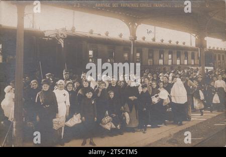 "Ankunft französischer Zivilflüchtlinge, Genf 1915" / "Arrivée des rapatriés civils Francais, Genève 1915": Große Gruppe von Menschen auf einem Bahnsteig neben einem Zug. Die meisten Passagiere sind Frauen und Kinder. Eine Krankenschwester, weiß gekleidet mit einem roten Kreuz auf ihrer Uniform, steht nach vorne. Einige der Leute tragen Bündel von Sachen. Eine Person hält eine französische Trikolore-Flagge. Stockfoto