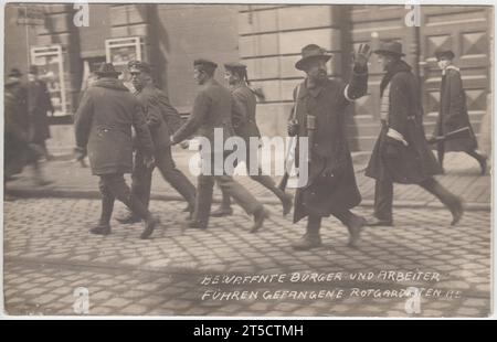 "Bewaffnete Bürger und Arbeiter vertrieben gefangengenommene Rote Garde" / "Bewaffnete bürger und arbeiter fahren gefangene rotgardisten": Nachwirkungen der Straßenkämpfe während der deutschen Revolution 1918-1919, nach dem Ersten Weltkrieg. Der Ort des Fotos ist unbekannt, aber es könnte München während des Umsturzes der Bayerischen Sowjetrepublik zeigen. Kommunistische Rote Garde, die von bewaffneten Männern in Zivilkleidung weggeführt werden. Ein bewaffneter Mann gibt jemandem Gesten aus der Kamera. Stockfoto