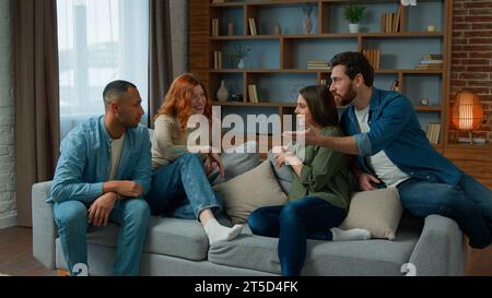 Ethnische Freunde sitzen auf der Couch im Wohnzimmer verschiedene Kollegen Teamkollegen Frauen Mädchen und Männer Lächeln sprechen über Pläne teilen freundliche Diskussion Stockfoto