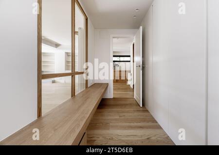 Flur eines Hauses mit weißen Holzschränken, einer langen Holzbank neben einem Oberlicht Stockfoto