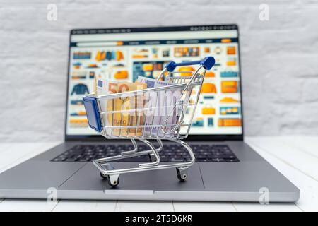 Augsburg, Bayern, Deutschland - 4. November 2023: Einkaufswagen mit Geldscheinen auf einem Laptop Computer vor einem Internet Online-Shop *** Einkaufswagen mit Banknoten auf einem Laptop vor einem Internet-Shop Credit: Imago/Alamy Live News Stockfoto