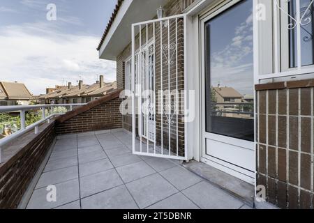 Kleine Terrasse mit weißem Geländer und weißem Steinzeugboden, Metallgeländer an Fenstern und Türen in einem Einfamilienhaus mit Blick auf die öffentlichen Bereiche Stockfoto