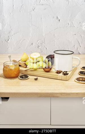 Stillleben mit frischem Obst auf einem Holzbrett neben einer Tasse Tee, einem Glas Marmelade und süßen Gewürzen Stockfoto