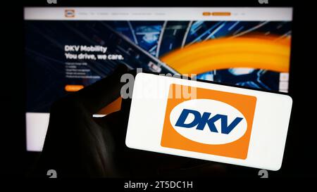 Person mit Smartphone mit Logo des deutschen B2B-Zahlungsunternehmens DKV Mobility vor der Website. Schwerpunkt auf dem Display des Telefons. Stockfoto