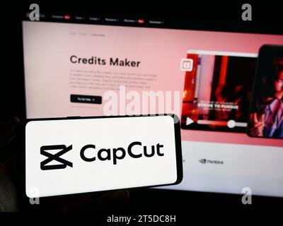 Person, die ein Mobiltelefon mit dem Logo der Videobearbeitungs-App CapCut vor der Unternehmenswebseite hält. Schwerpunkt auf dem Display des Telefons. Stockfoto