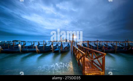 Italien, Venedig, Gondeln, die nachts am Embankment vertäut sind, mit einsamem Licht auf dem nassen Holzpier. Stockfoto