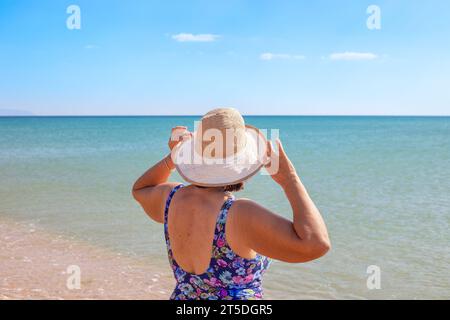 Eine Dame mit Hut und Badeanzug ruht an einem sonnigen Sommertag am Meer. Stockfoto