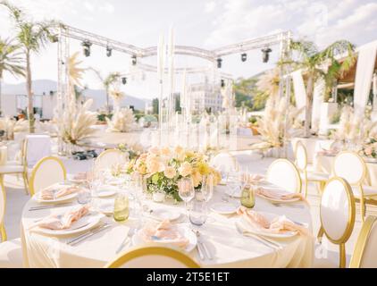 Auf der Freiluftterrasse stehen überdachte festliche Tische mit Blumensträußen und Kerzen Stockfoto