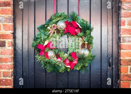Detail eines Weihnachtskranzes an einer alten schwarzen Holztür eines Landhauses, Großbritannien Stockfoto