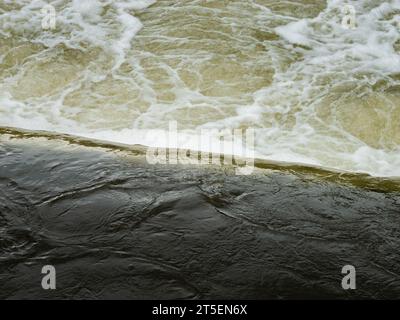 Das Wasser dampft aus einem Wehr und bildet eine Menge Blasen. Auf der Wasseroberfläche befindet sich Schaum. Die Turbulenzen mischen Luft in Wasser. Stockfoto