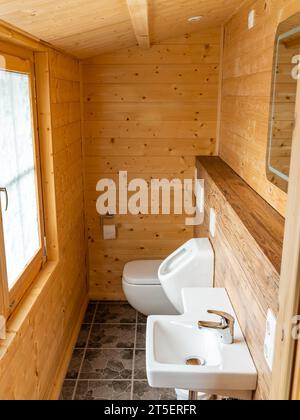 Badezimmer in einem Holzgebäude. Weißes Waschbecken, Urinal und Toilette. Innenarchitektur in einem kleinen Haus oder einer kleinen Hütte, die als Sommerhaus genutzt wird. Stockfoto