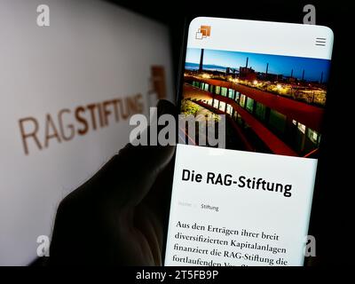 Handyhalter mit Website der RAG-Stiftung vor Logo. Konzentrieren Sie sich auf die Mitte des Telefondisplays. Stockfoto