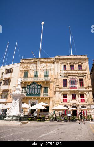 Vittoriosa, Malta - 17. Juni 2023: Sonnenschirme mit Bartischen auf dem Platz in Vittoriosa unter den Gebäuden Stockfoto