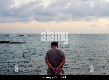 Rückansicht eines Mannes, der am Strand nachdenkt. Rückansicht eines Mannes, der am Strand nachdenkt Stockfoto