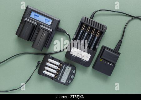 Verschiedene Ladegeräte für verschiedene Batterietypen. Nahaufnahme auf hellgrünem Hintergrund, Draufsicht. Stockfoto