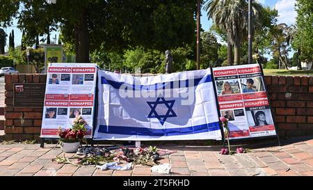 Plakate von von der Hamas entführten Menschen und eine israelische Flagge am Eingang des Caulfield Park in Melbourne, mit Blumen vor der Ausstellung Stockfoto