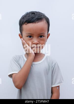 Porträt eines kleinen asiatischen Jungen, der seine Wange mit Zahnschmerzen hält. Leiden an Zahnschmerzen im Mund Stockfoto