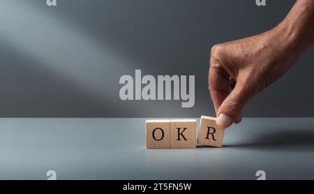 OKR, Objektive, Schlüssel, Ergebnisse, Hand Putting Holzwürfelblöcke mit Text OKR auf graublauem Hintergrund. Konzept des Geschäftsziels und der Leistung. Stockfoto