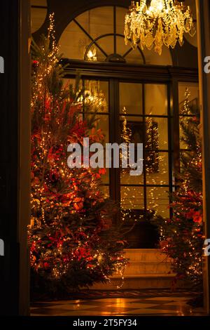 Es ist ein klassisches Weihnachtsbild mit roten Weihnachtsbäumen, einem antiken Kronleuchter an der Decke und einer Glastür im Hintergrund. Stockfoto
