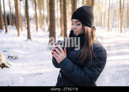 Schöne Frau denkt an heißen Kaffee aus der Thermoskanne im verschneiten Wald Stockfoto