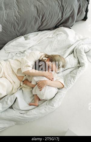 Das kleine Mädchen legt sich auf ihre Mutter und will schlafen. Mom umarmt ihre Tochter zärtlich. Vertikaler Rahmen. Stockfoto