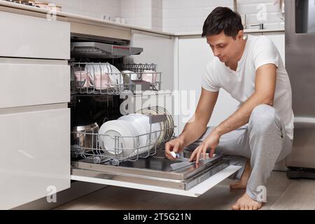 Hübscher Mann, der Waschmitteltablette in der Küche in den Geschirrspüler bringt Stockfoto