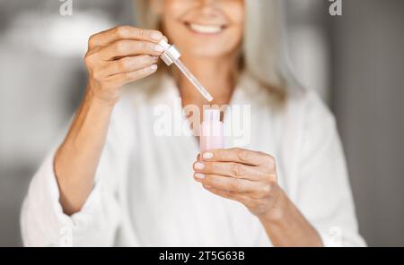 Hautpflege. Lächelnde Reife Frau, Die Flasche Mit Feuchtigkeitsspendendem Gesichtsserum Hält Und Öffnet Stockfoto
