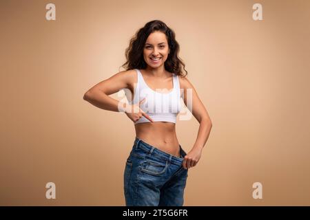 Glückliche attraktive brünette schlanke Millennial-Frau in riesigen Jeans Stockfoto