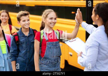 Schwarze Lehrerin gibt High-Fives für Kinder, die in den Schulbus steigen Stockfoto