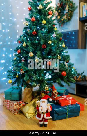 Santa und Elfen Figuren in der Nähe von bunten Geschenken, die auf dem Boden unter dem Weihnachtsbaum liegen Stockfoto