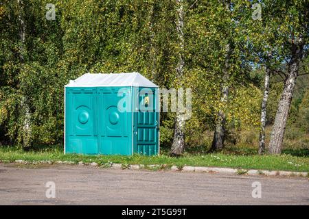 Grüne mobile öffentliche Toilette für Behinderte steht am Straßenrand vor Birkenbäumen. Stockfoto