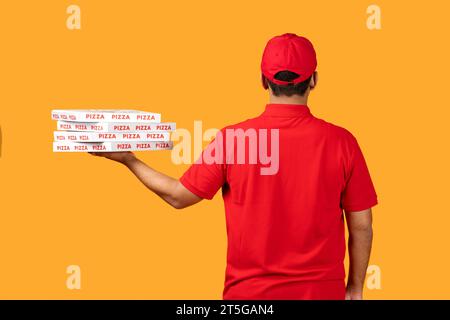 Rückansicht des Kuriers, der Pizzakartons vor gelbem Hintergrund hält Stockfoto