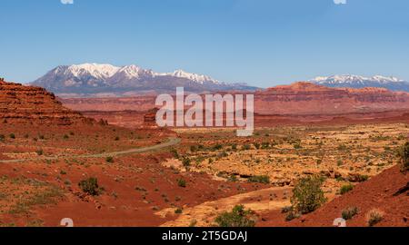 Panoramablick auf eine Wüstenstraße im Süden von Utah, USA, mit schneebedeckten Bergen am Horizont und klarem blauem Himmel. Stockfoto