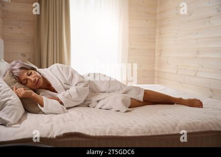 Die alte Frau schläft in einem hellen Schlafzimmer auf einem großen Bett Stockfoto