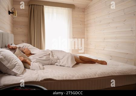 Ältere Frau ruht in einem hellen Schlafzimmer auf einem großen Bett Stockfoto