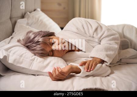 Ältere Frau schläft in einem hellen Schlafzimmer auf weichen Kissen Stockfoto
