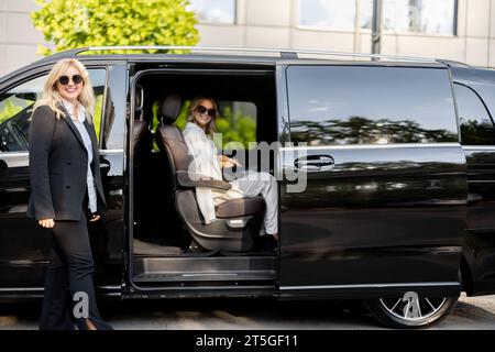 Weibliche Chauffeurin hilft Geschäftsleuten, aus einem Fahrzeug auszusteigen Stockfoto