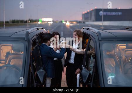 Gruppe von Geschäftspartnern, die nachts mit Alkohol in der Nähe von Autos feiern Stockfoto
