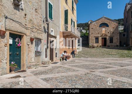 Platz und Kirche Sant'Agostino im alten Steindorf der italienischen Riviera mit Touristen im Frühling, Borgio Verezzi, Savona, Ligurien, Italien Stockfoto