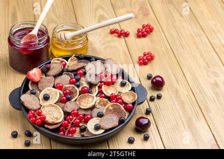 Pfannkuchen und Beeren in der Pfanne. Honig und Marmelade auf dem Tisch. Heller Holzhintergrund. Draufsicht. Kopierbereich Stockfoto