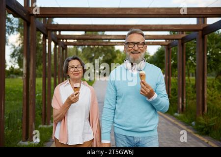 Fröhliches Seniorenpaar isst Eisbecher im Park und genießt entspannte Zeit Stockfoto