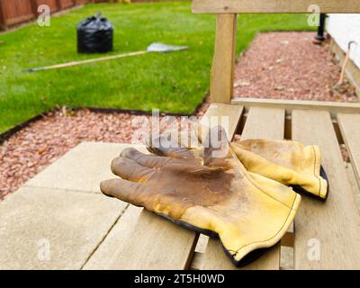 Gartenhandschuhe auf Gartensitz und gebarkte Blätter in schwarzer Tasche Stockfoto